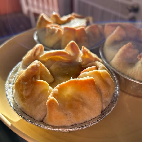 Close-up of several golden-brown HI Pie Bakery + Cafe mini pies in foil cups on a yellow tray.
