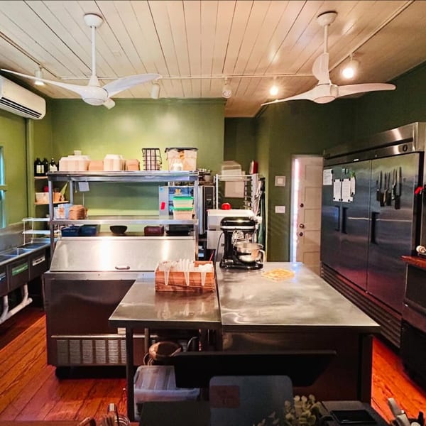 A clean, well-lit bakery kitchen with stainless steel counters, appliances, and a stand mixer.
