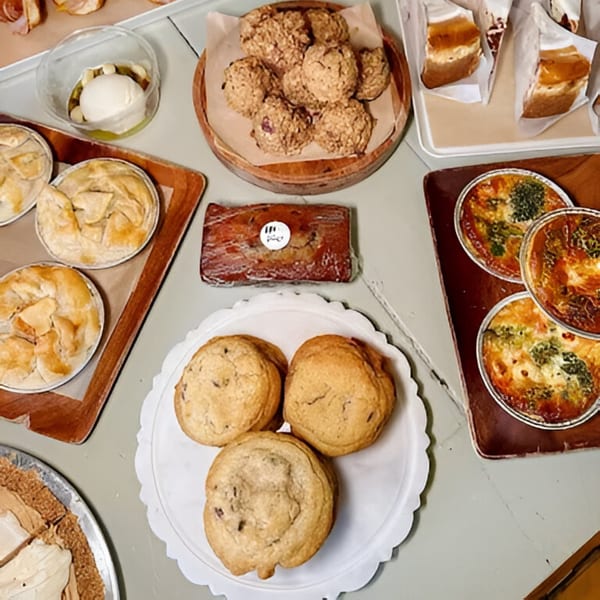 An overhead view of various baked goods, including pies, cookies, quiches, and cakes, on a light-colored surface.