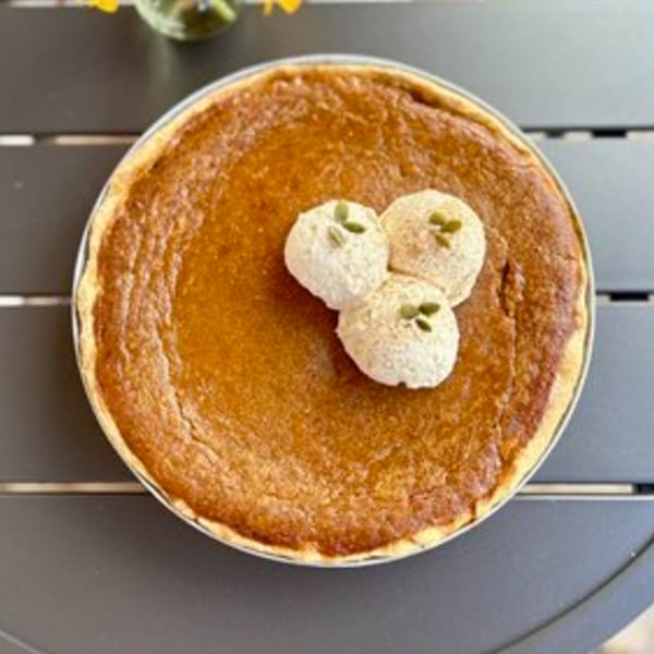 A whole pumpkin pie from HI Pie Bakery + Cafe, topped with three dollops of whipped cream and pumpkin seeds.