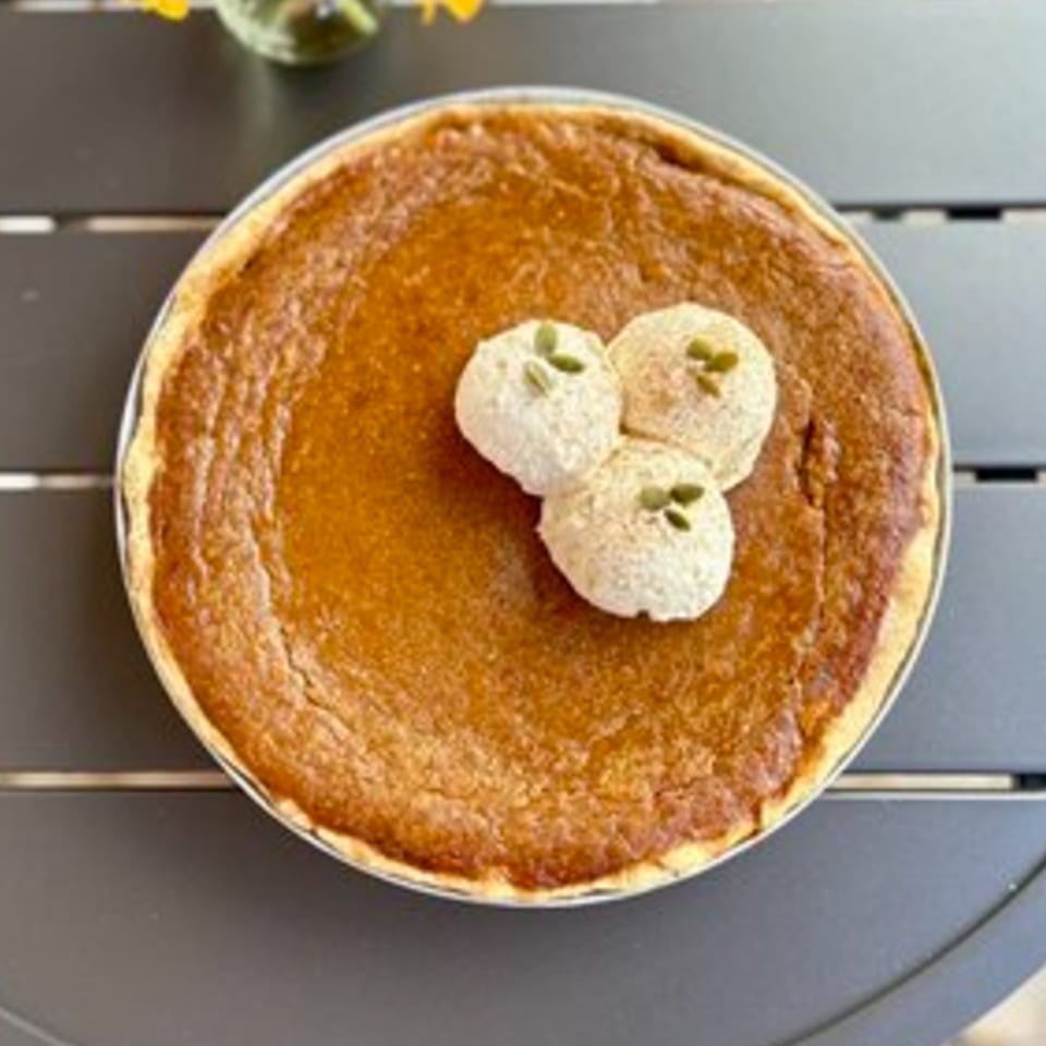 A whole pumpkin pie from HI Pie Bakery + Cafe, topped with three dollops of whipped cream and pumpkin seeds.