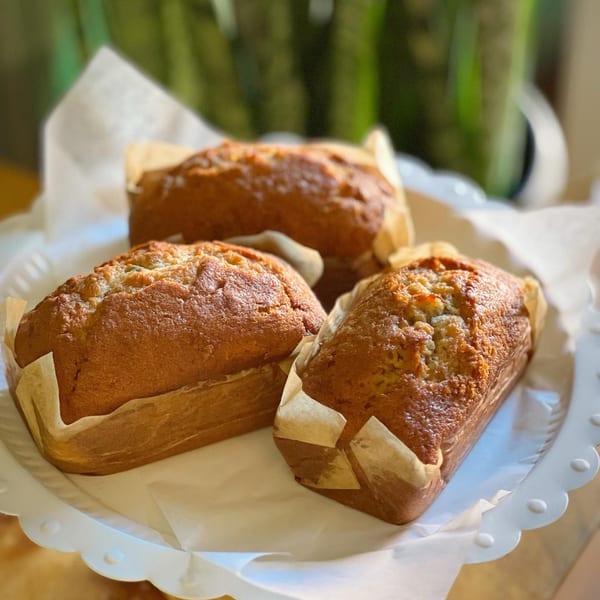 Three golden-brown mini banana bread loaves in parchment paper on a white scalloped tray.