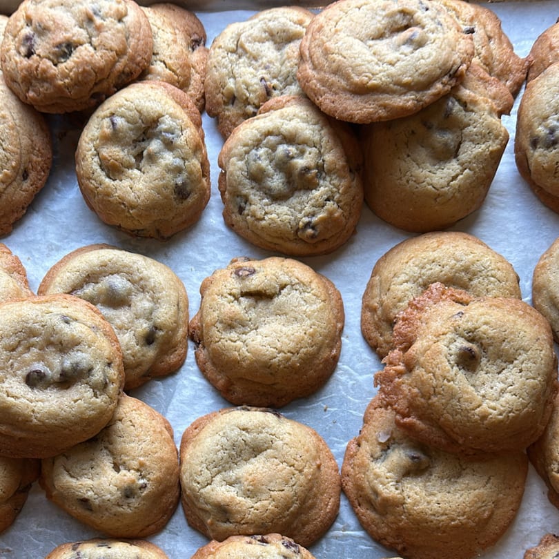 Freshly baked chocolate chip cookies with golden-brown edges and soft centers, arranged on parchment paper.