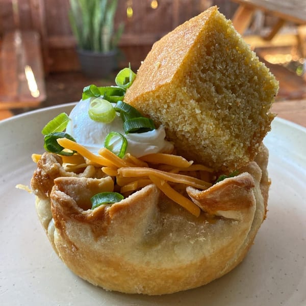 Savory pie with shredded cheese, sour cream, green onions, and a slice of cornbread.