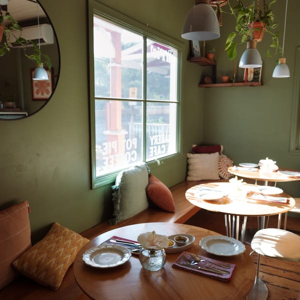 Cozy HI Pie Bakery + Cafe interior with green walls, wooden tables, and sunlit window seating.