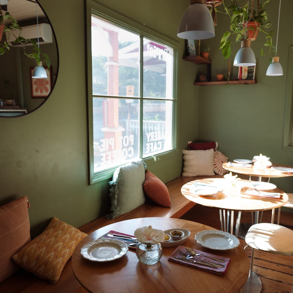 Cozy HI Pie Bakery + Cafe interior with green walls, wooden tables, and sunlit window seating.