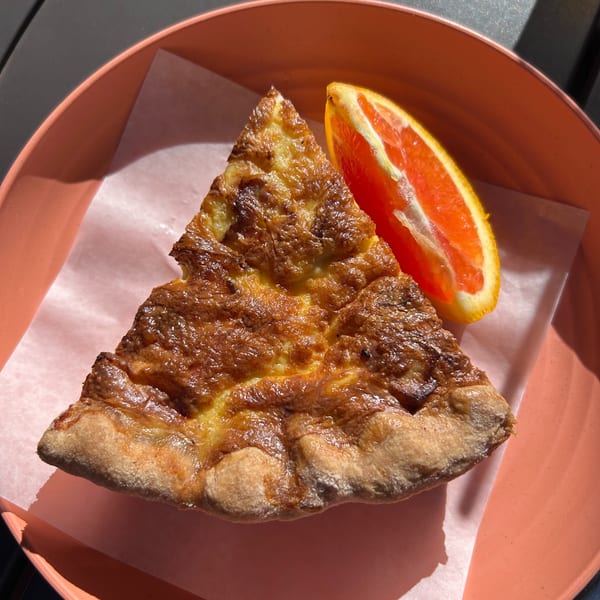 A slice of golden-brown quiche with a side of grapefruit on a pink plate at HI Pie Bakery + Cafe.