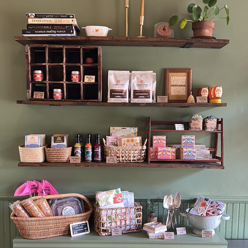 A retail display with shelves of coffee, hot sauce, cards, honey, and baked goods in a cafe.