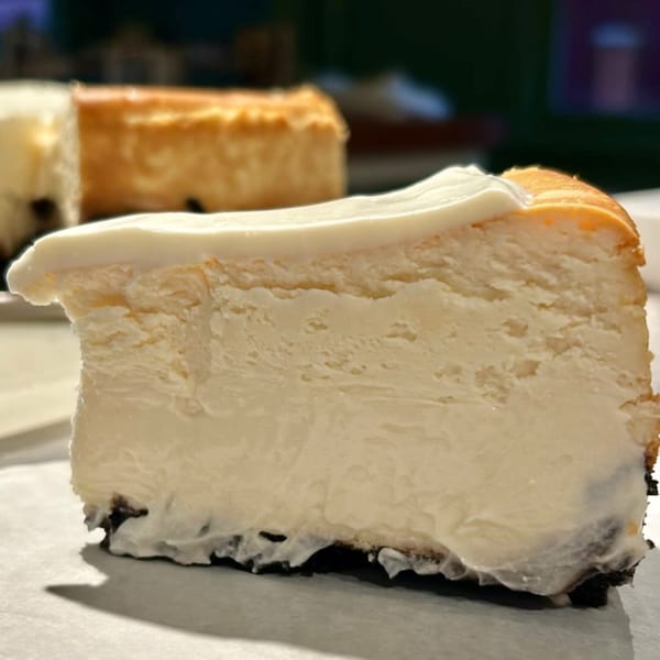 A close-up of a slice of HI Pie Bakery + Cafe cheesecake with a dark crust and white topping.
